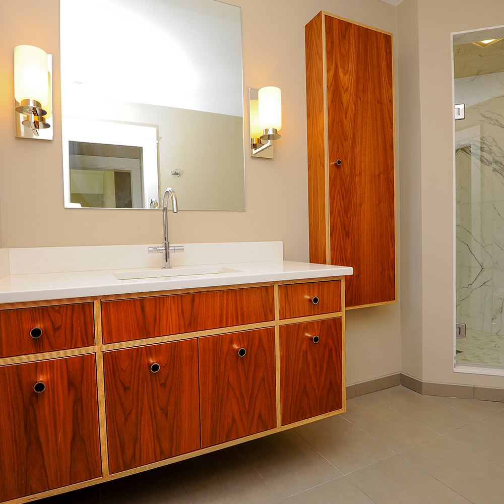 Modern bathroom in Wells, Maine, with wooden cabinets, white countertop, a large mirror, and wall-mounted lights.