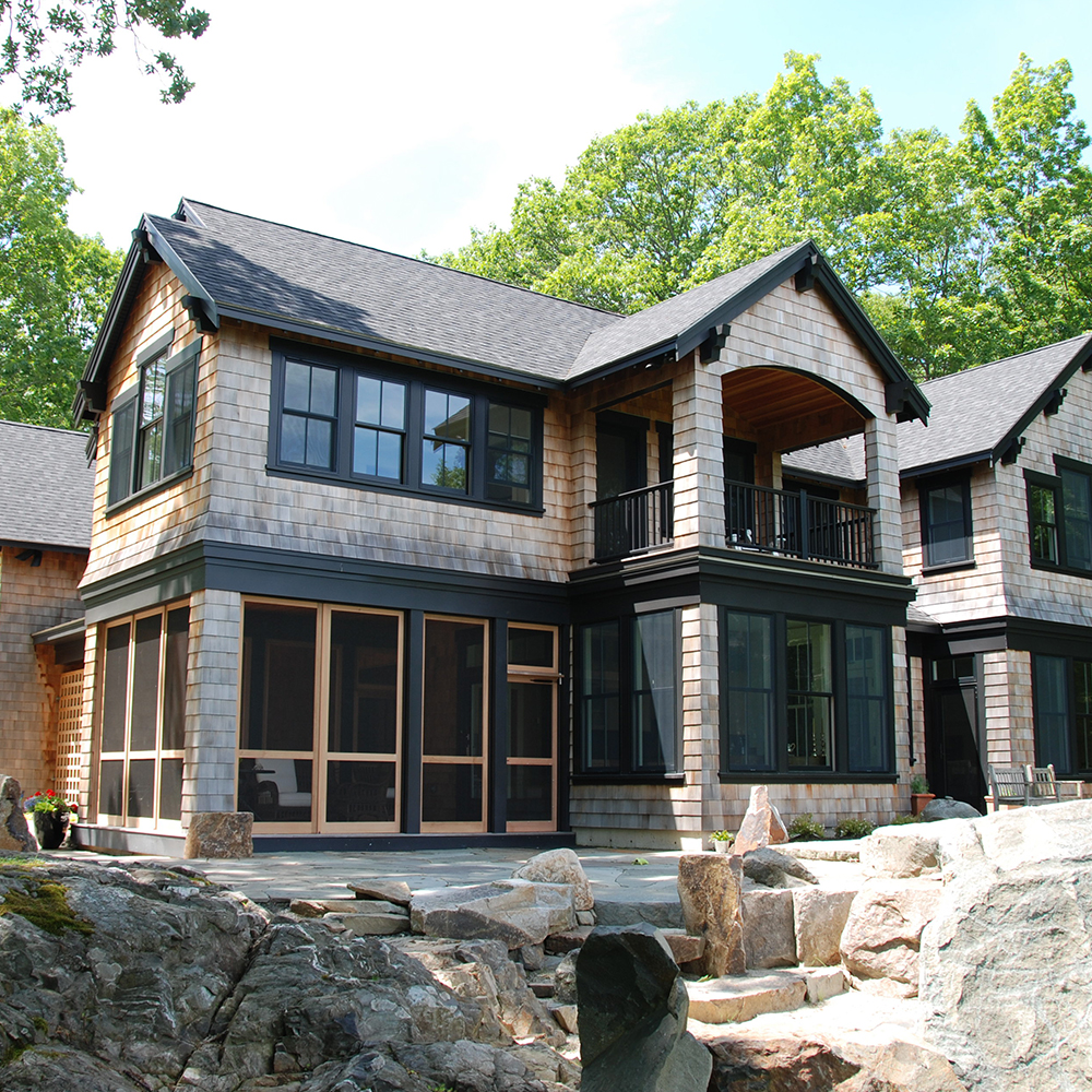 A modern two-story house with a stone base, large windows, and a combination of shingle and wood siding, enhanced by recent home remodeling, surrounded by trees.
