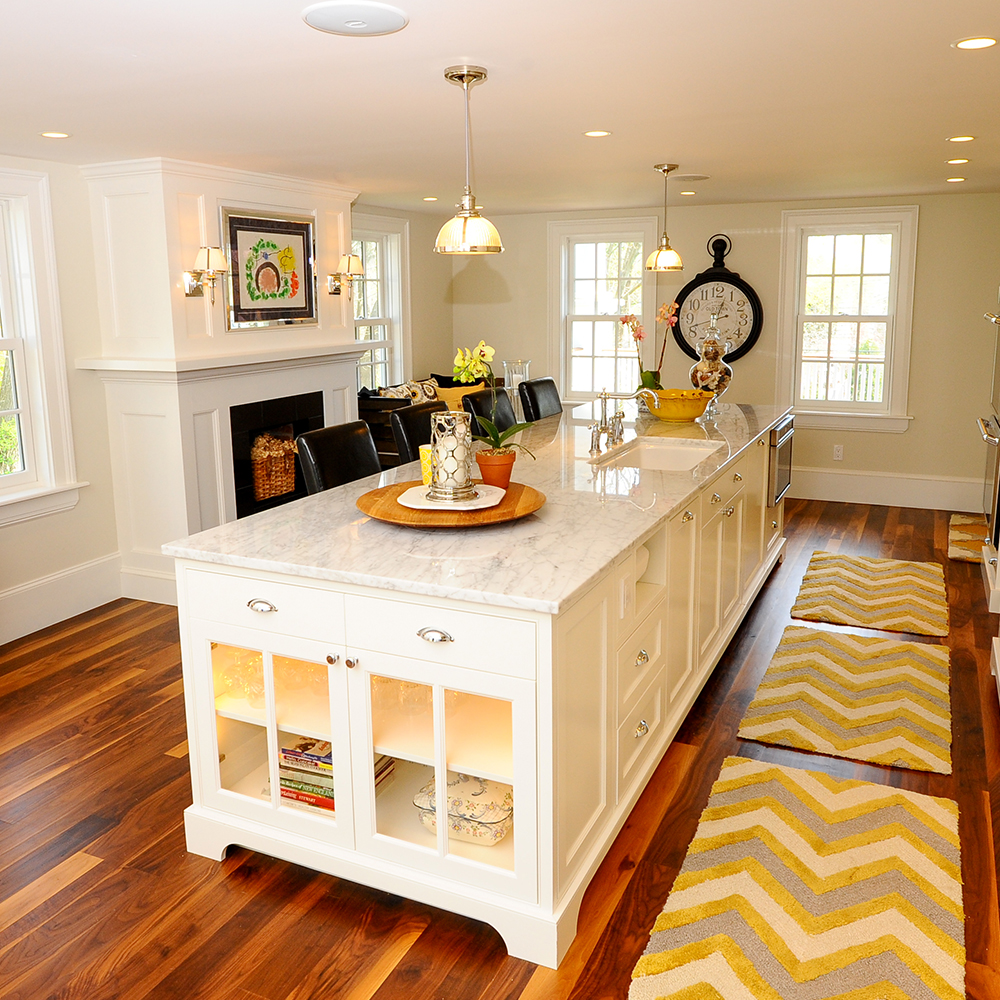 Bright kitchen with white cabinets, marble island, pendant lights, and a wooden dining area in the background, customized for a Maine home.