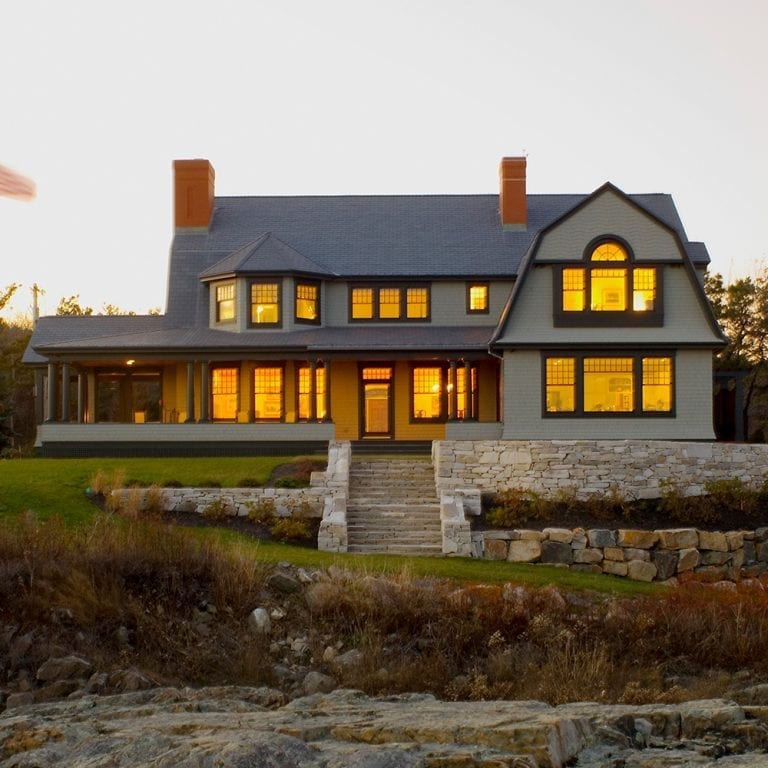 A large two-story home with lit windows at twilight, featuring a stone pathway and surrounding natural landscape.