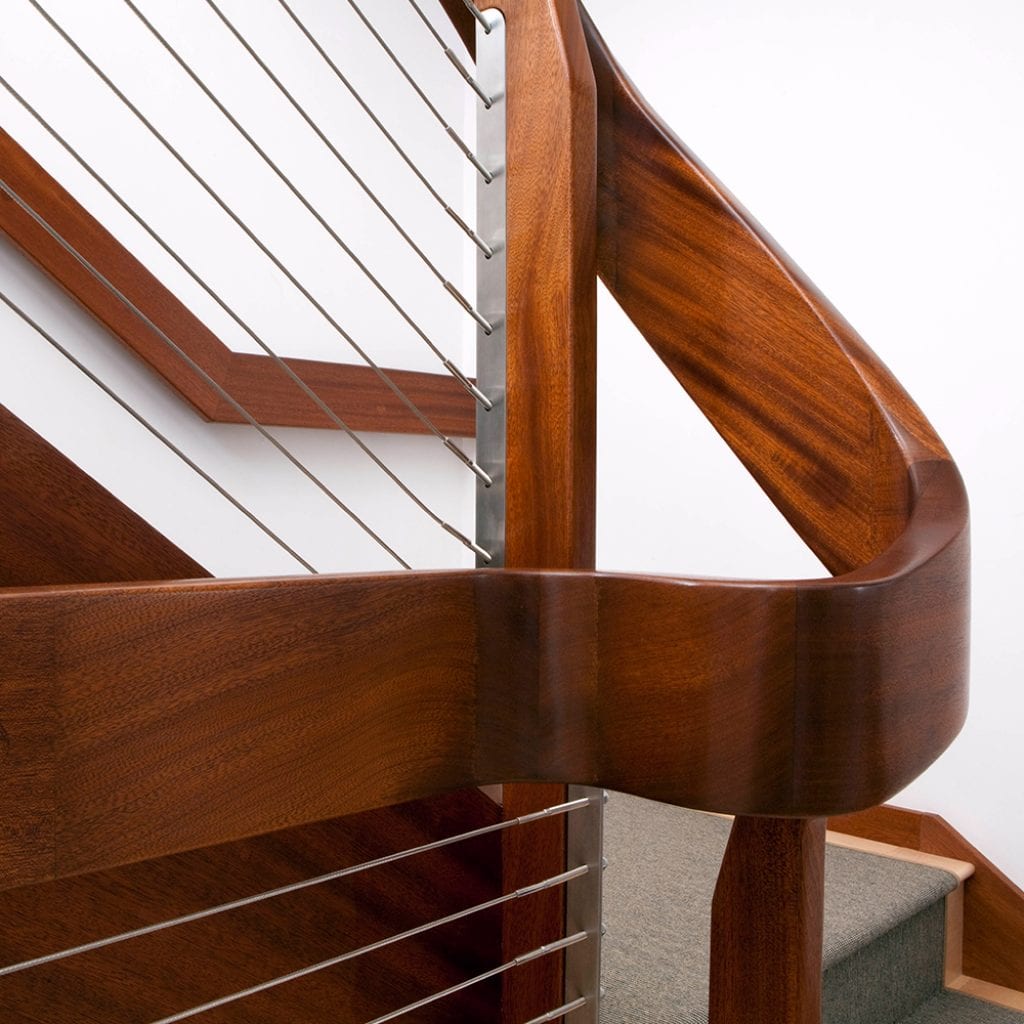Close-up of a modern wooden staircase with a curved handrail and metal balusters against a white background, designed by Wells home builders for custom homes.
