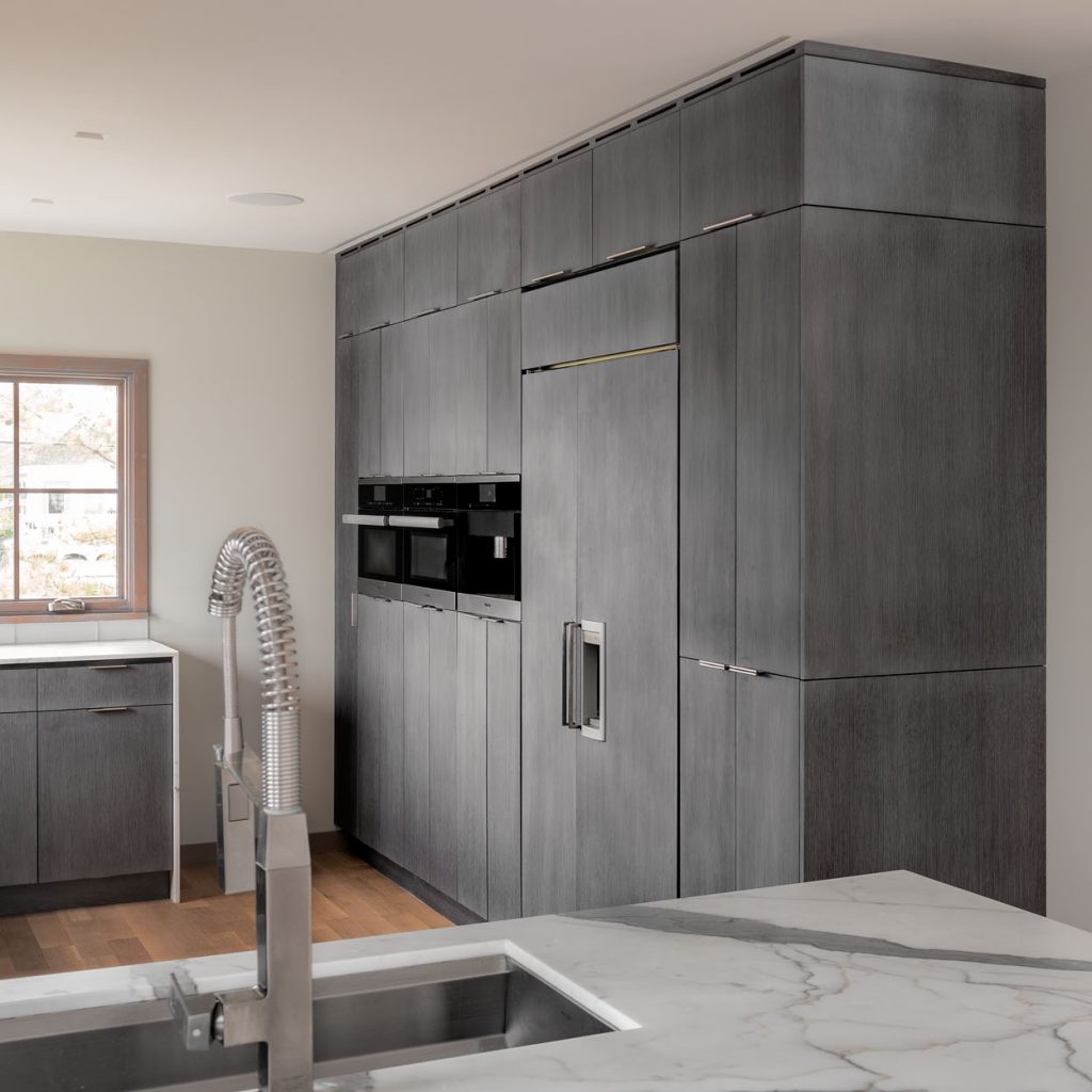 Modern kitchen interior with sleek gray cabinetry featuring built-in appliances and a large marble kitchen island with a professional Wells sink faucet.