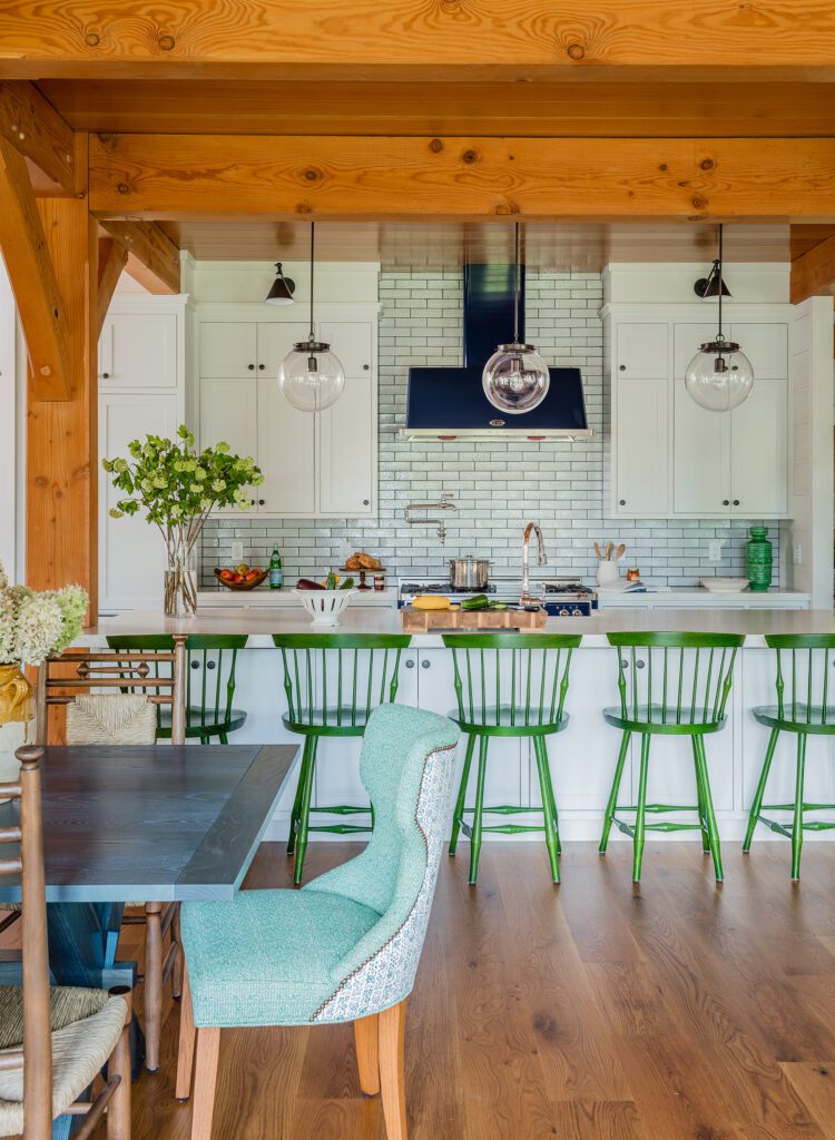 Bright, modern kitchen with white cabinetry, a brick backsplash, and green bar stools at a central island in Wells, Maine, complemented by exposed wooden beams and hardwood floors.