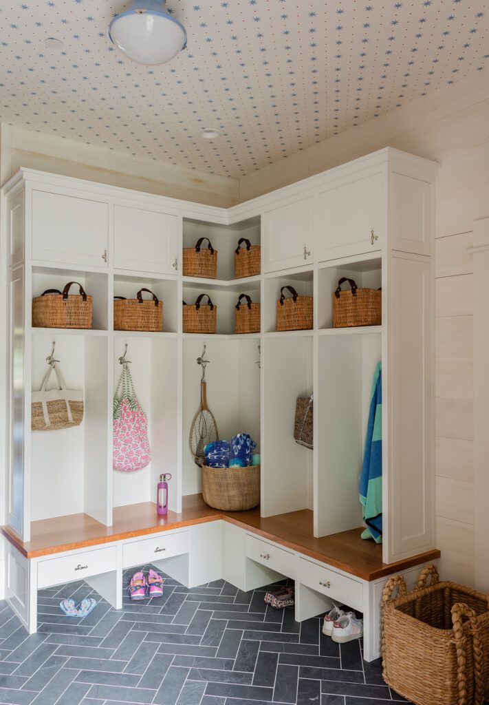 A well-organized mudroom in custom homes, featuring white built-in cabinets, benches, and hooks, decorated with baskets and hanging beach towels.