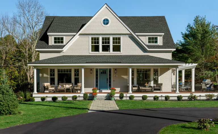 A large two-story home with a gray shingle exterior, white trim, and a covered front porch, surrounded by manicured lawns and mature trees in Maine.