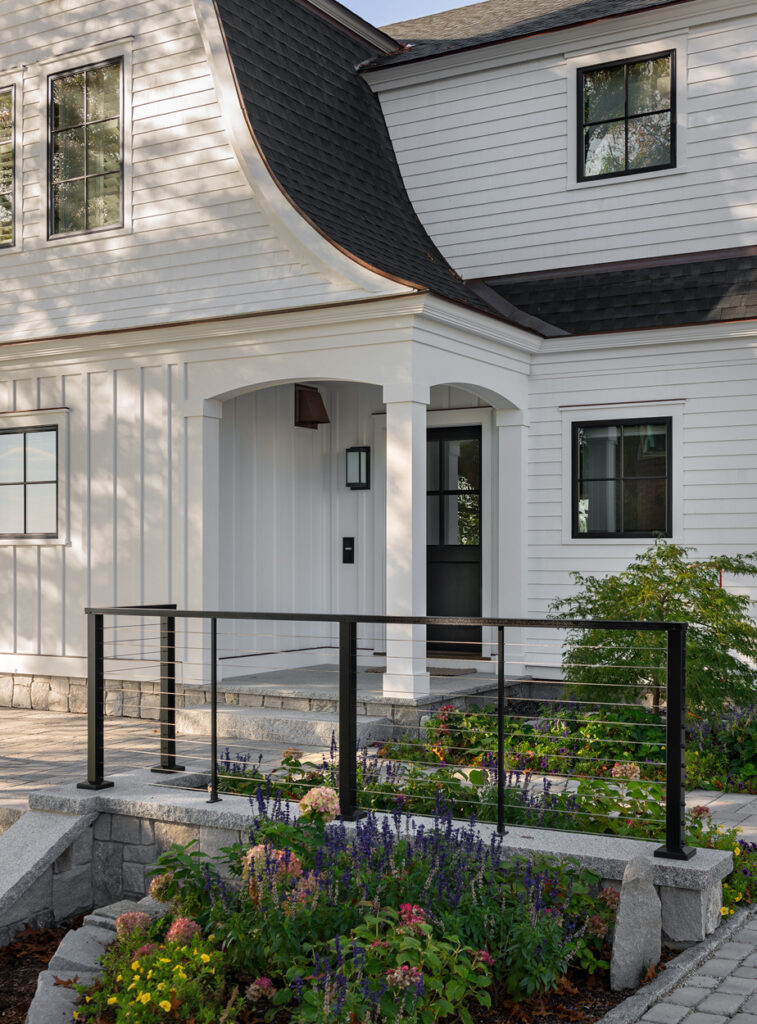 Exterior view of a custom home with white siding, arched entryway, and a landscaped garden with colorful flowers and a stone pathway.