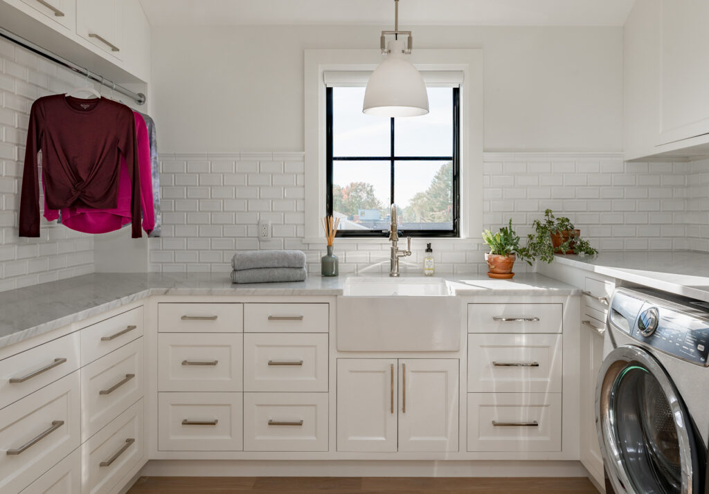 Modern laundry room with white cabinets, stainless steel appliances, and a pink shirt hanging near the window, recently updated by home remodeling.