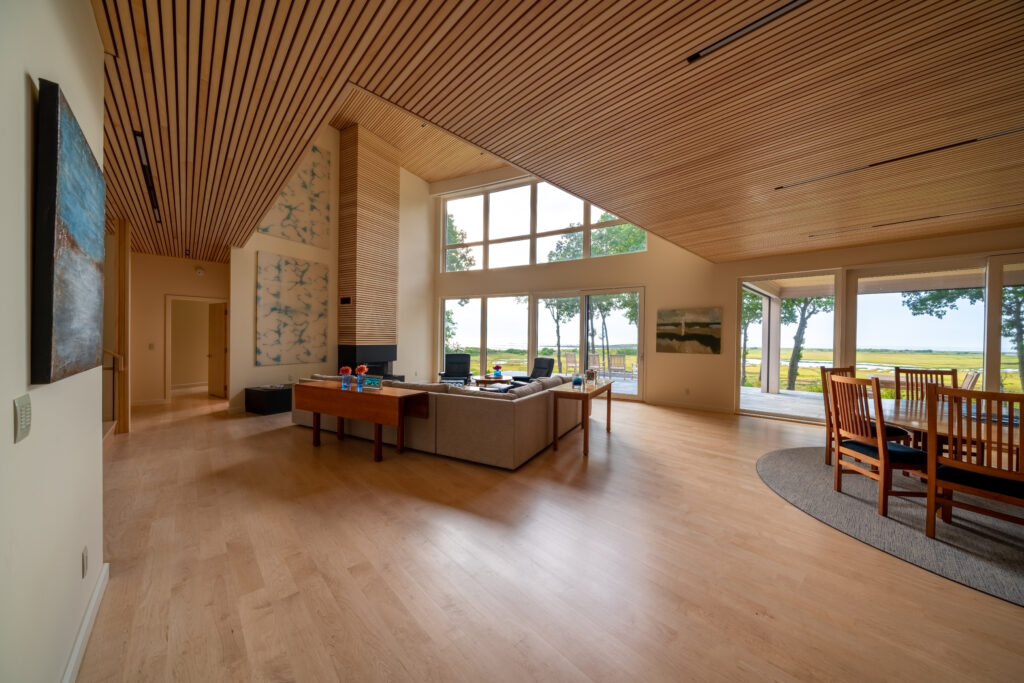 Spacious living room with wooden slat ceiling, large windows overlooking a lawn in Maine, modern furniture, and wall art.