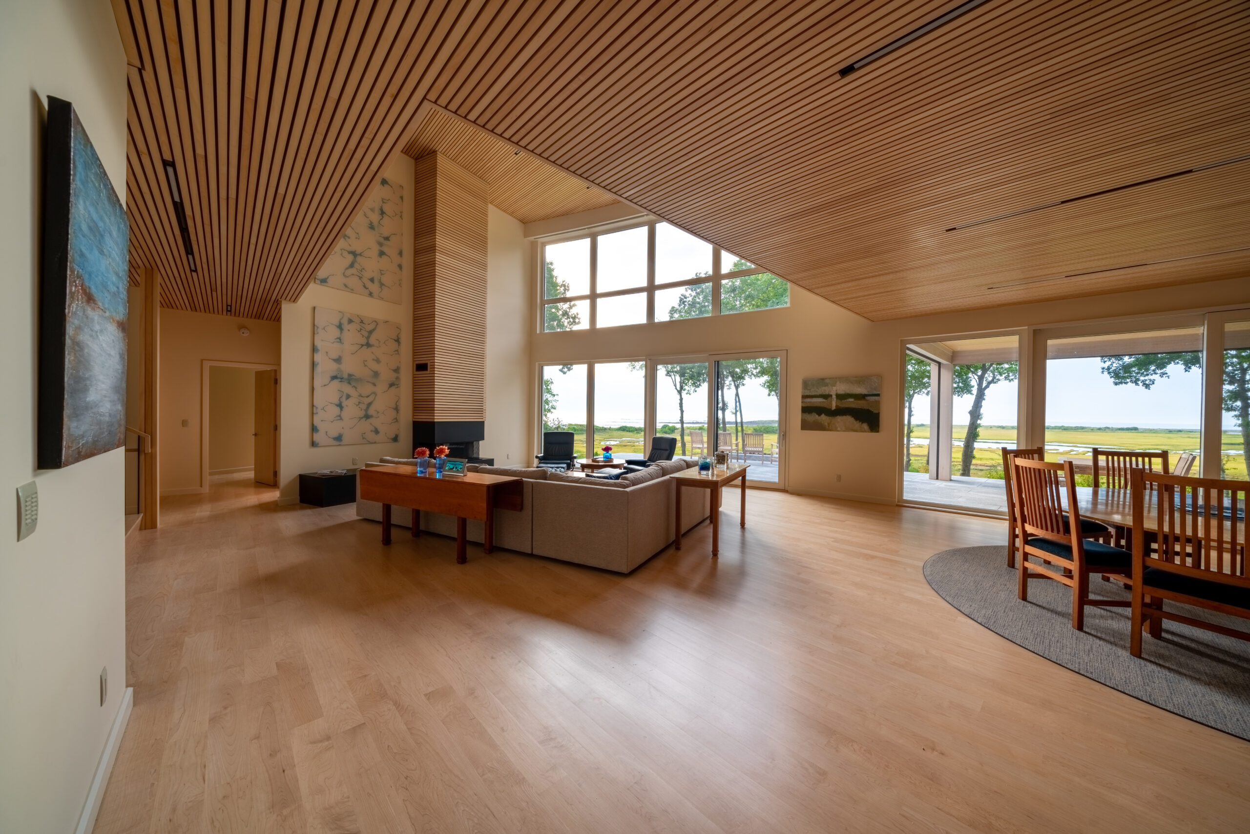 Spacious living room with wooden slat ceiling, large windows overlooking a lawn in Maine, modern furniture, and wall art.