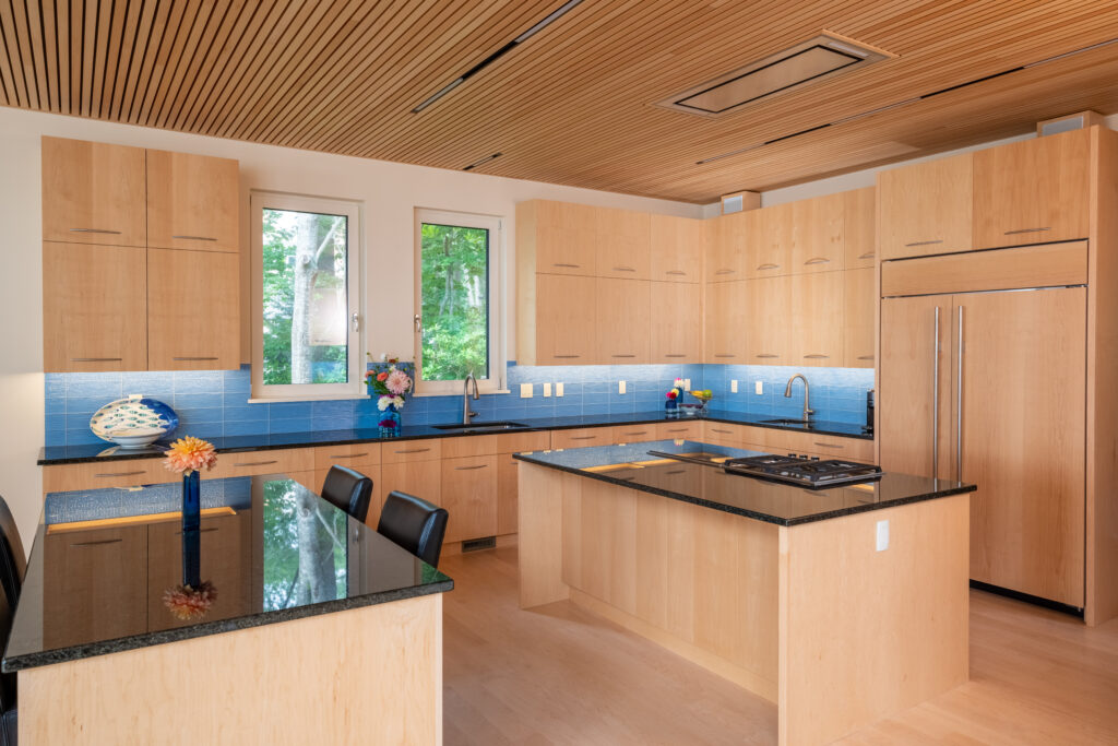 Modern kitchen with wooden cabinets, blue tile backsplash, stainless steel appliances, and a central island with a black countertop, designed by Wells home builders.