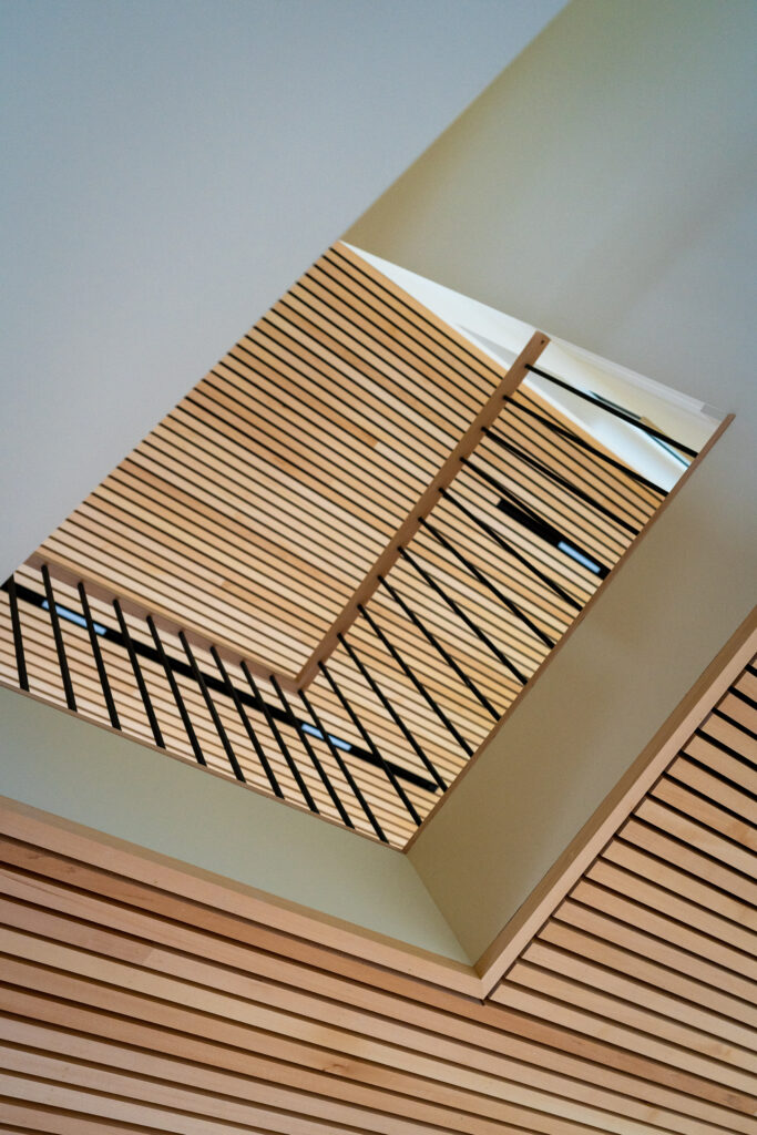 Modern architectural detail of a staircase in a custom home, viewed from below, showing angular wooden slats against a bright, clear sky.