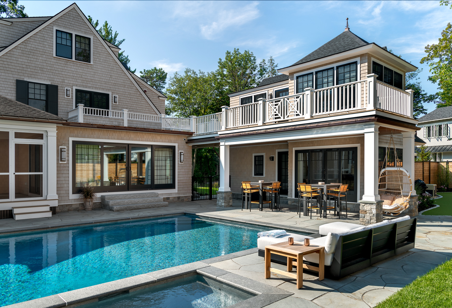 Luxurious backyard with a swimming pool in Wells, Maine, flanked by two custom homes, featuring a furnished patio area and lush landscaping.