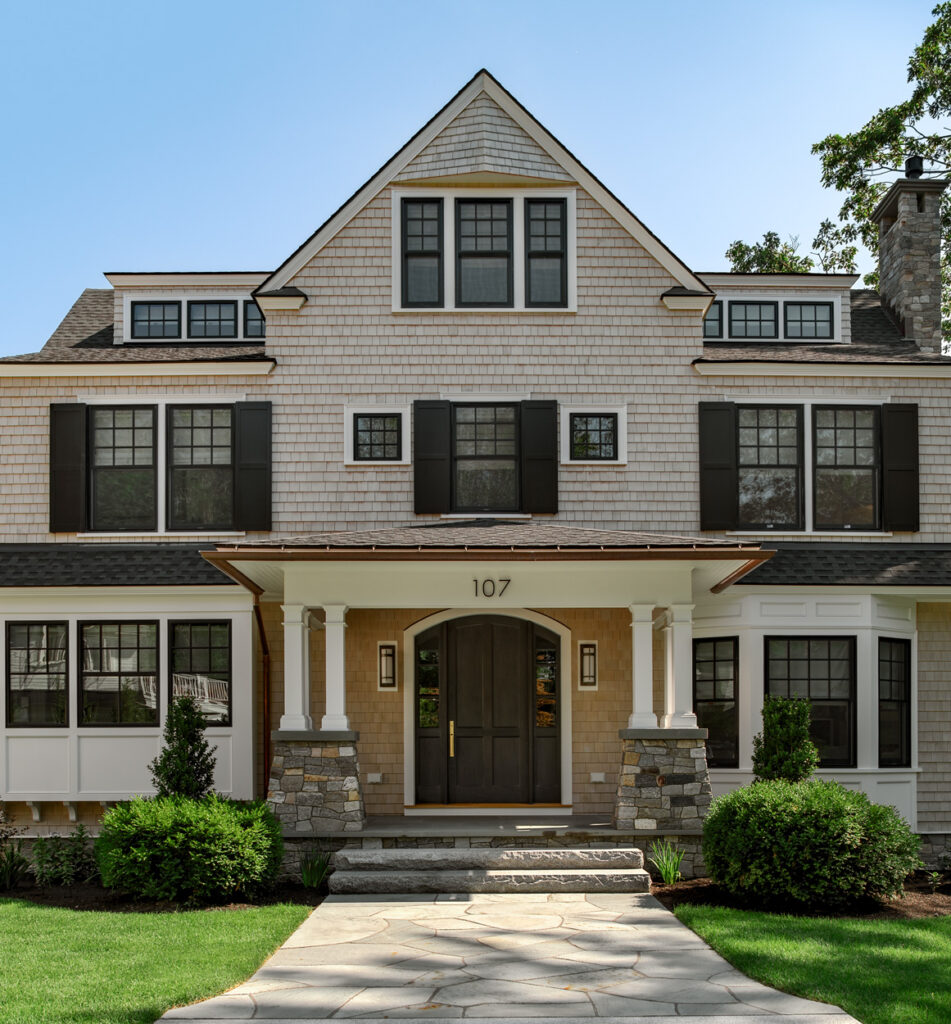 Large two-story house in Wells, Maine with a symmetrical design featuring a centered entrance, stone foundation, and shingled facade under a triangular gable.