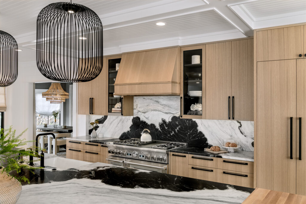 Modern kitchen with light wood cabinets, black marble countertops, and hanging black wicker lamps in a custom home.