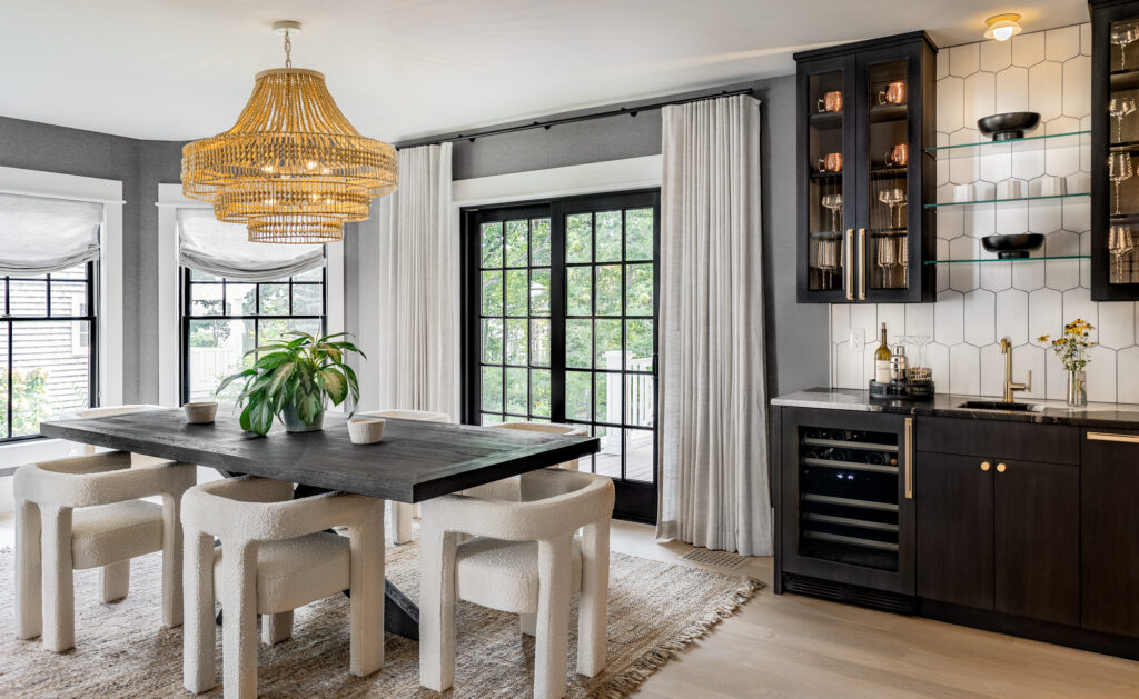 Modern kitchen with a chandelier over a dining table, black cabinetry, and a large window with curtains, ideal for home remodeling in Maine. Decor includes plants and patterned tiles.