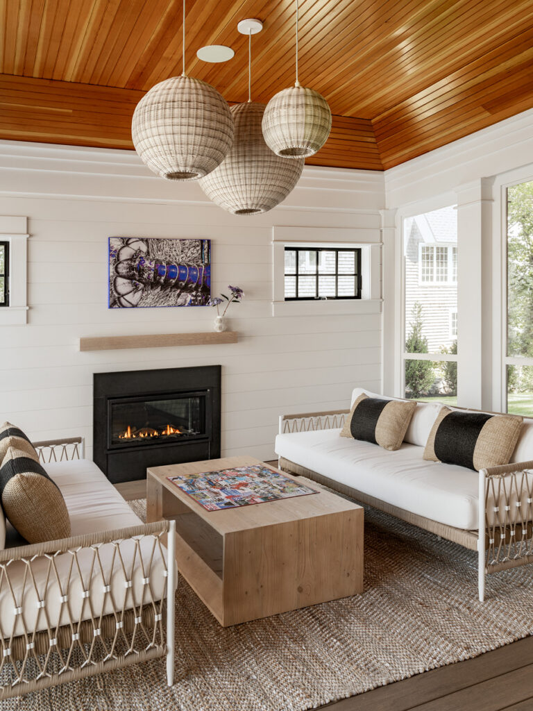 Cozy living room featuring a fireplace, white sofas with pillows, wooden coffee table, and hanging spherical lamps under a renovated wooden ceiling.